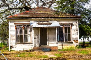 An aged home with peeling paint, overgrown landscaping, and a sagging front porch